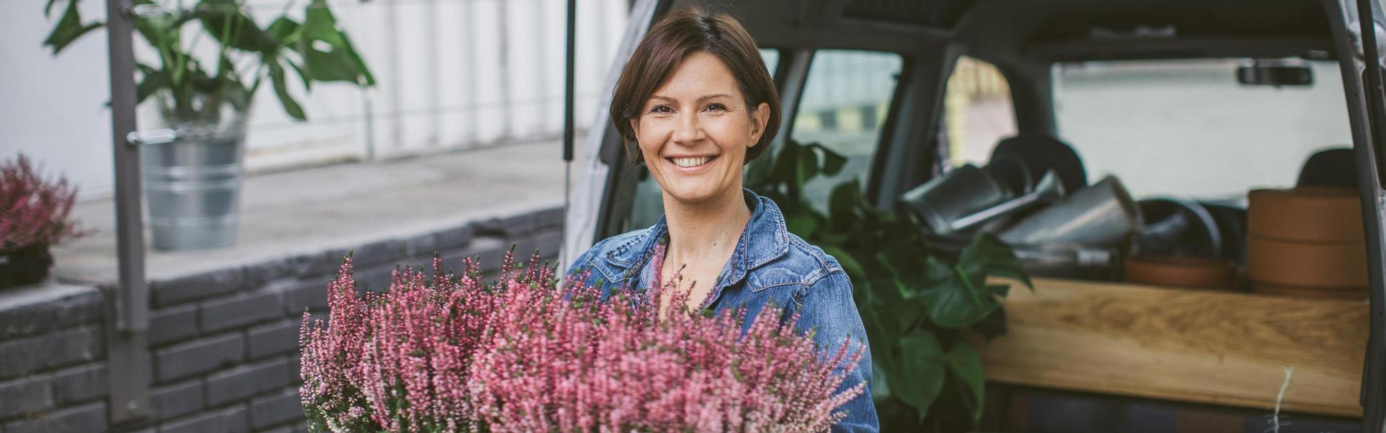 Smiling woman loading car trunk filled with different type of flowers.