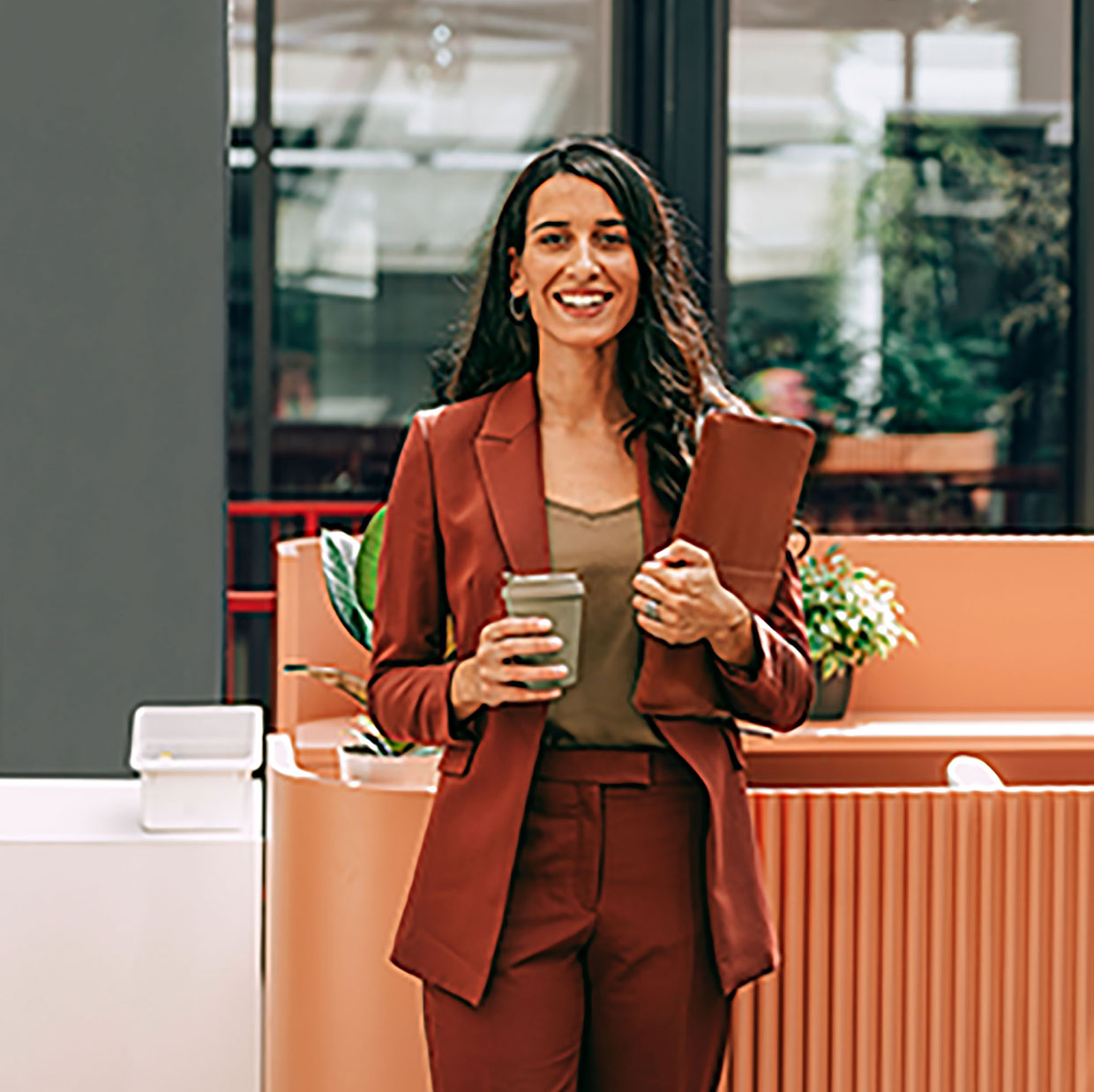 Kvinna i röd kostym som håller i en kaffekopp och en mapp